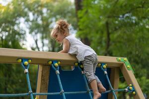 Little Caucasian girl plays on playground climbs stairs upstairs. photo