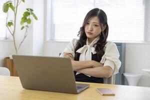 un preocupado japonés mujer por remoto trabajo en el pequeño oficina foto