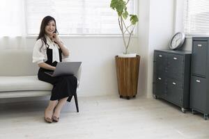 un japonés mujer comprobación teléfono inteligente por remoto trabajo en el hogar oficina foto