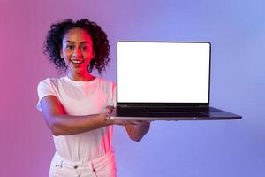 Smiling black woman presenting open laptop with blank screen, colorful background photo