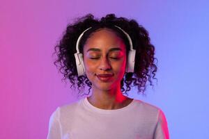 Content black lady with headphones enjoying music on neon background photo