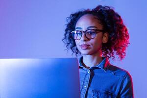 Focused black woman with glasses working on laptop with blue lighting photo