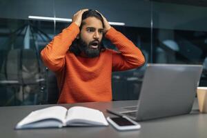 Shocked millennial eastern businessman in dark office photo