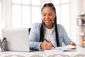 Happy black lady student studying with laptop at home photo