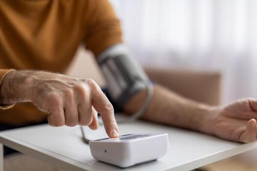 Pensioner using modern tonometer, pressing button on device, photo