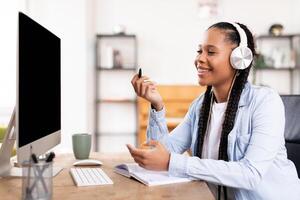 alegre negro dama con auriculares estudiando a computadora foto