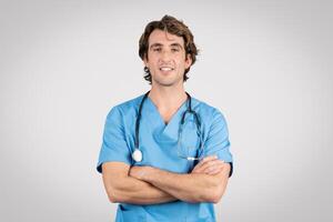 Confident male nurse in blue scrubs with arms crossed and stethoscope photo