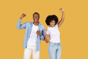 Enthusiastic African American couple celebrating success with arms raised and fists clenched photo
