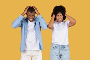 Stressed young couple with hands on their heads, eyes closed, and faces contorted in frustration photo