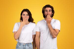 man and a woman with surprised expressions, both covering their mouths with their hands photo