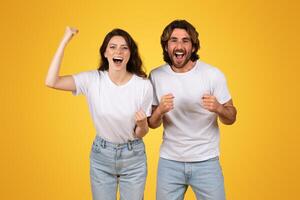 Energetic young couple with raised fists celebrating a victory, exuding joy and excitement photo