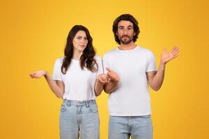 Confused young couple with raised hands, showing uncertainty and questioning gestures photo