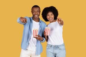 Joyful African American couple in casual clothing holding red and white striped popcorn boxes photo