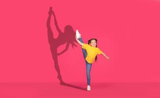 A joyful young girl in a yellow shirt and jeans performs a high leg kick with enthusiasm photo
