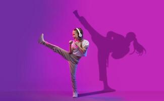 A vibrant young girl with headphones joyfully kicks high into the air, her silhouette casts a dancing photo