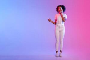 Smiling black lady pointing to side at free space on blue and pink gradient background photo