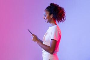 Happy black lady with smartphone and earbuds on pink and purple background photo