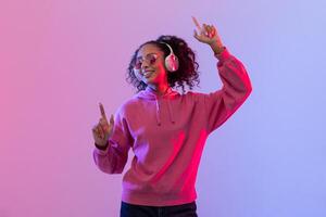 Joyful african american woman dancing with headphones in neon light photo