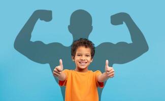 An exuberant young boy in an orange t-shirt gives two thumbs up photo