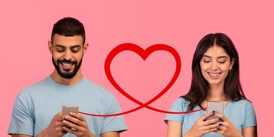 A man with a beard in a blue t-shirt smiles at his phone while a woman with long hair in a similar blue top looks at hers photo