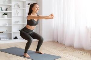 Energetic asian woman performing squats exercise at home photo