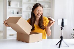 Cheerful asian vlogger presenting new cosmetic product from an open box photo