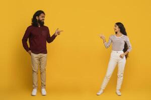 Man and woman pointing each other on yellow background photo