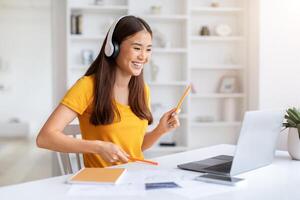 alegre asiático mujer vistiendo auriculares teniendo divertido mientras utilizando ordenador portátil foto