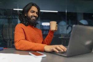 Happy man with cup engaging with laptop photo