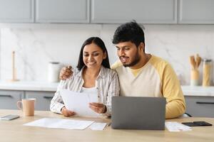 Happy young indian spouses reading letter from bank, kitchen interior photo