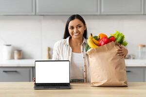 Happy young indian woman order grocery online, showing laptop photo