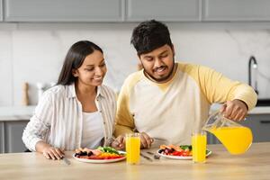 Loving happy eastern couple have breakfast together in kitchen photo