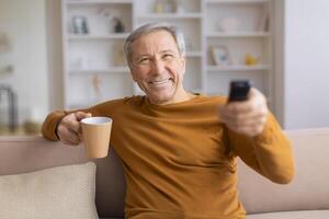 Senior man with coffee mug changing TV channels photo