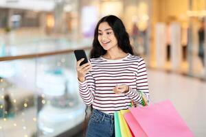 emocionado indio dama con teléfono inteligente y compras pantalones foto