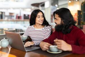 Positive young indian couple using laptop at cafe photo