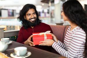 hermosa joven indio hombre y mujer intercambiando regalos a café foto