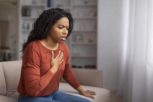 preocupado joven negro mujer sufrimiento dolor en cofre mientras sentado en sofá foto