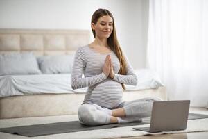 Calm Young Pregnant Woman Having Online Yoga Lesson With Laptop At Home photo