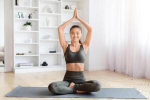 Peaceful young asian woman in activewear practicing yoga at home photo