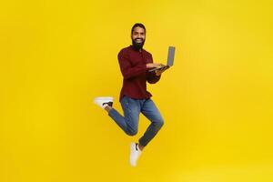 Excited eastern man with laptop jumping on yellow background photo