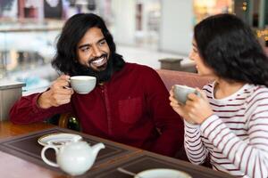 Cute affectionate indian couple sitting at table in city cafe photo