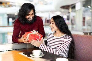 Loving indian guy giving his girlfriend birthday gift at cafe photo