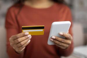 Young black woman holding credit card and using her smartphone at home photo