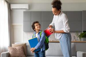 Mother preparing son for school with backpack photo