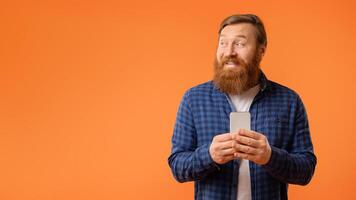 bearded man holding phone looking aside at blank space, studio photo