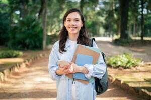 Radiant young female student holding books and a smartphone, looking optimistic photo