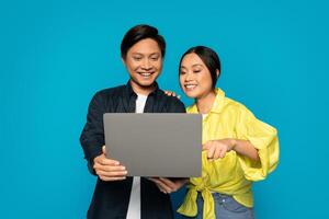 Enthusiastic Asian couple collaboratively working on a laptop with attentive and joyful expressions photo