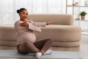 Positive expecting black lady stretching body at home photo