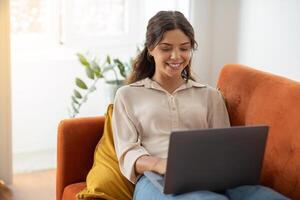 Online Communication. Young Female Using Laptop While Sitting On Couch At Home photo