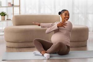 Pregnant african american woman sitting on yoga mat, stretching arms photo